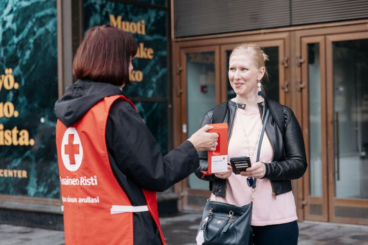 Alt-teksti: Nälkäpäivän lipaskerääjä ojentaa lippaan ohikulkijalle kadulla.