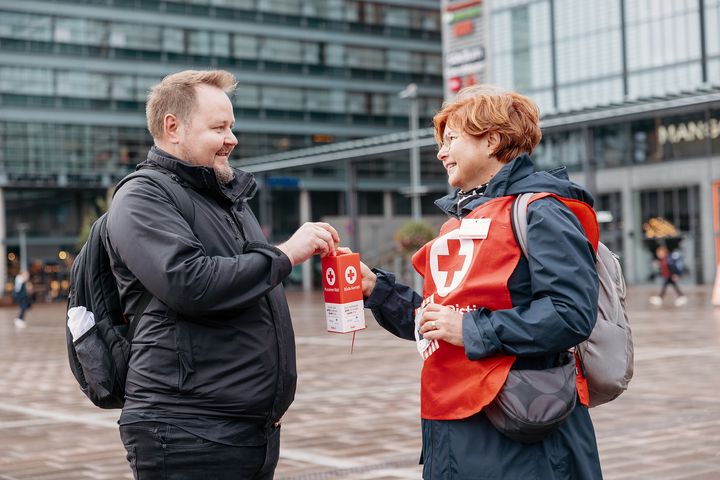 Nälkäpäivän lipaskerääjä ja henkilö, joka laittaa rahaa lippaaseen.