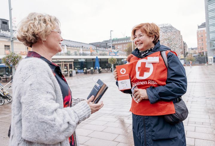 Två personer samtalar under Hungerdagens insamling i Finland. En av dem bär en väst med Finlands Röda Kors logo.