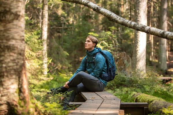 Nuori mies istuu pitkospuiden päällä metsässä.