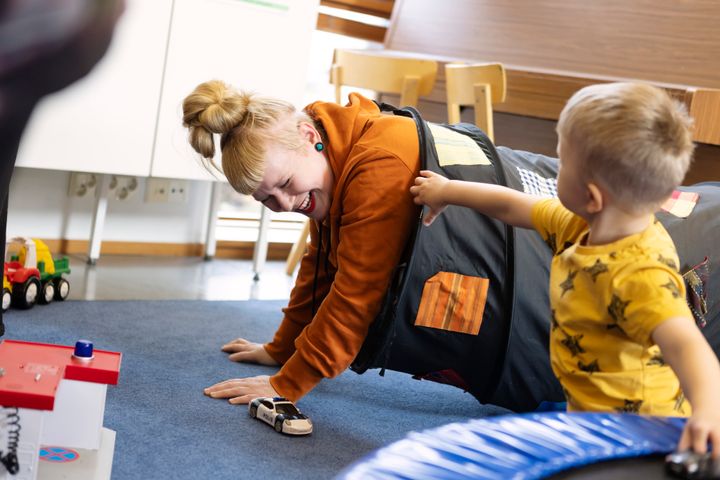 Pieni lapsi ja hänen äitinsä leikkivät Leikkipuisto Linjan lattialla Kalliossa. Äiti on leikkitunnelissa ja nauraa, lapsi ojentaa hänelle pikkuautoa.