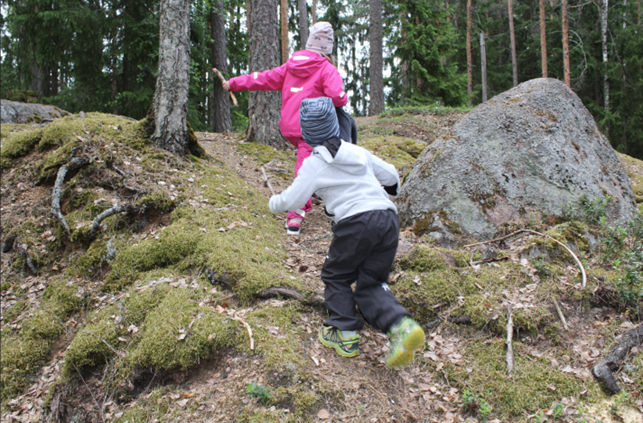 Kaksi lasta juoksevat metsässä selkä kameraan.