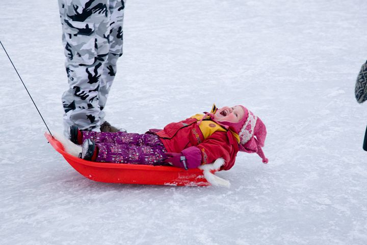 Pieni lapsi nauraa istuen pulkassa jäällä.