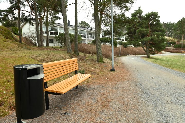 Keltainen levähdyspenkki ja roskis rantaraitin varrella.