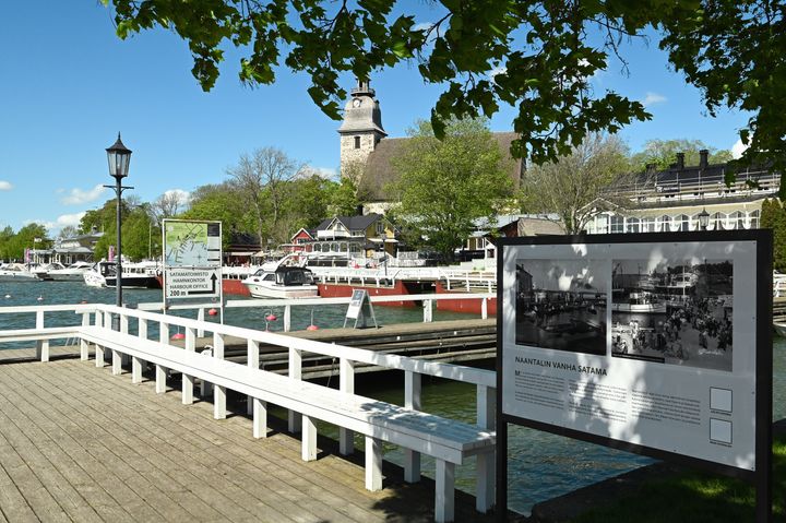 Naantalista kertova historiataulu Naantalin rannassa. Taustalla kirkkomaisema.