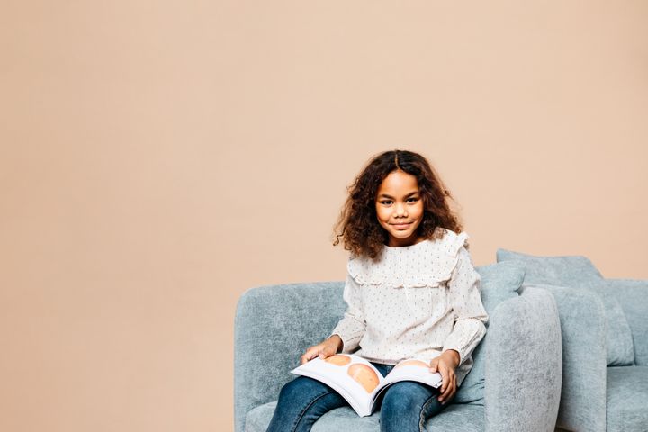 Nuori tyttö lukee kirjaa ja istuu nojatuolilla.