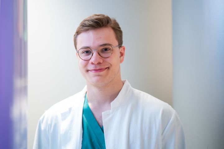 Aleksanteri Asikainen in a white coat, wearing glasses, standing indoors.