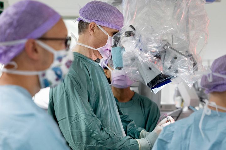 Surgical team in green scrubs and masks performing a neurosurgery, using advanced equipment.