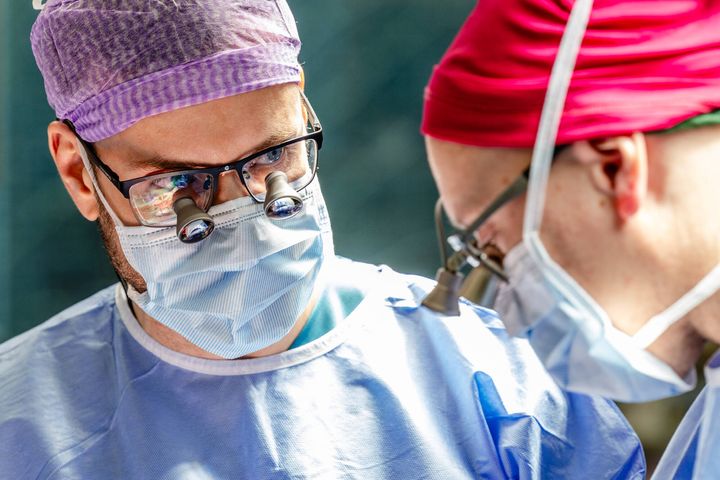 Two surgeons wearing surgical attire and magnifying glasses during a procedure.