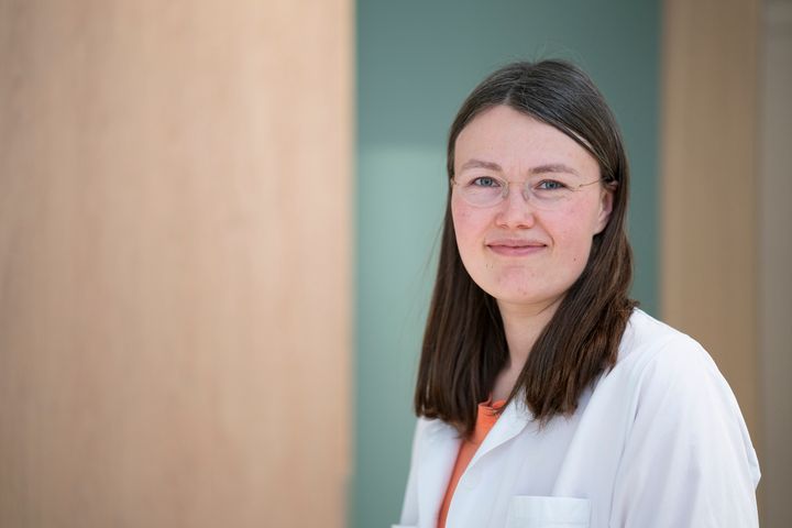 Person in a white coat smiling in an indoor setting.