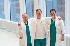 Kolme lääkäriä seisoo yhdessä hymyillen käytävällä sairaala-asuihin pukeutuneina.