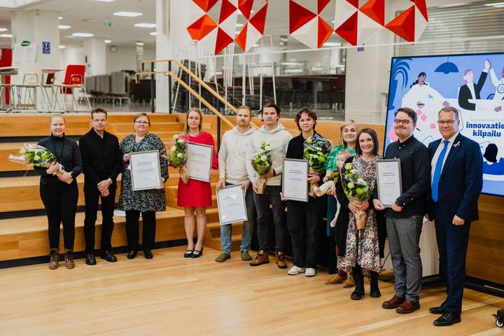 En grupp på 11 personer poserar med hedersbevis och blommor i händerna.