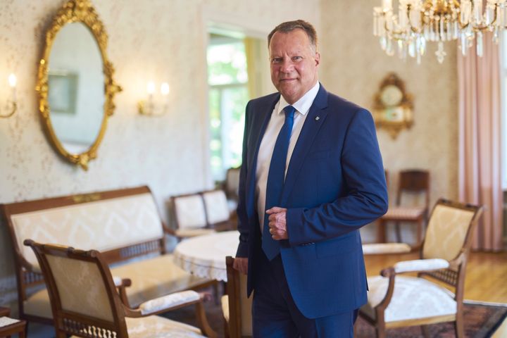 A man in a blue suit stands in an elegant room with vintage furniture and decor.