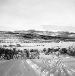 Luminen maisema Nuorgamista, jossa näkyy latuja etualalla, taloja keskellä ja lumipeitteisiä vuoria taustalla.