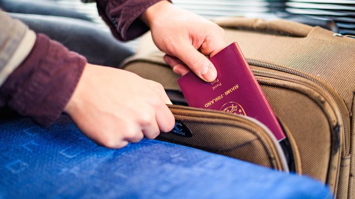 Henkilö laittaa passin matkalaukun taskuun.