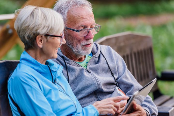 Vanhempi pariskunta istuu penkillä ulkona ja katsoo yhdessä tablettia.