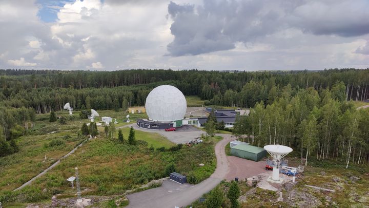 Satelliittiantenneja metsäisellä alueella, keskellä suuri valkoinen pallomainen antenni.