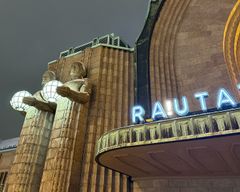 View of a building with statues holding spherical lights and partially visible neon sign reading "RA!UTATIEASEMA".