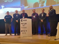 "Six people standing on a stage next to a podium with 'ESA Phi-Lab NET Finland' sign."