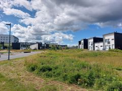 Nykyajan asuinalue, jossa on uusia niittyjä ja moderneja rakennuksia pilvisen taivaan alla.