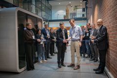 Kuvassa joukkio ihmisiä sisätiloissa seisomassa rivissä. Kaksi henkilöä keskellä leikkaa nauhaa saksilla.