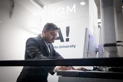 Mies työskentelee tietokoneella laboratoriossa, taustalla tekstit "IQM" ja "Aalto University".