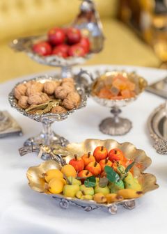 A table with ornate silver dishes holding walnuts, candy, and decorative fruit.