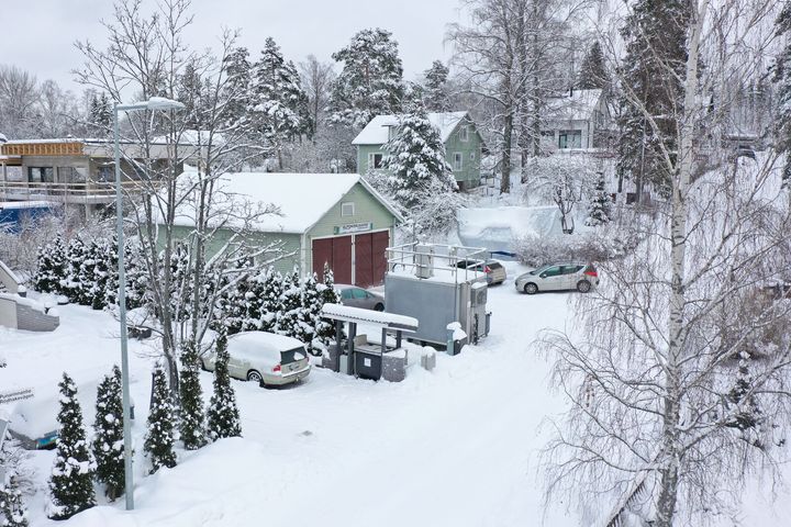 Rakennuksen edessä, tienvarrella seisoo harmaa kontti, jossa on mittalaitteita katolla.