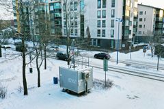 Harmaa mittausasema sijaitsee kadun varressa.