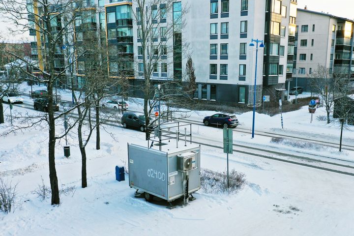 Harmaa mittausasema sijaitsee kadun varressa.