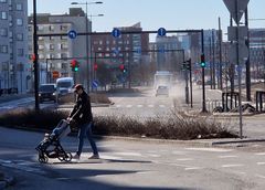 Henkilö kävelee lapsen kanssa kävelytietä pitkin kadulla, jossa näkyy katupölyä.