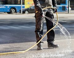 Henkilö kastelee katua letkulla vähentääkseen pölyn muodostumista hiekan poiston aikana.