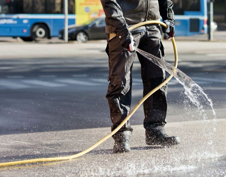 Henkilö kastelee katua letkulla vähentääkseen pölyn muodostumista hiekan poiston aikana.
