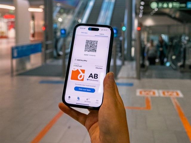 Asiakas pitää kädessään puhelinta, jossa näkyy sovelluksesta ostettu lippu metrolaiturille menevien liukuportaiden edessä
