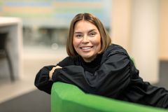 Annemari Airaksinen, S-Pankki / Nainen hymyilemässä, nojaa vihreää sohvaa vasten.