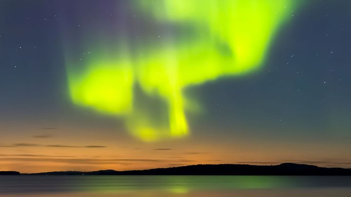 Revontulet loistavat värikkäästi yötaivaalla järven yllä.