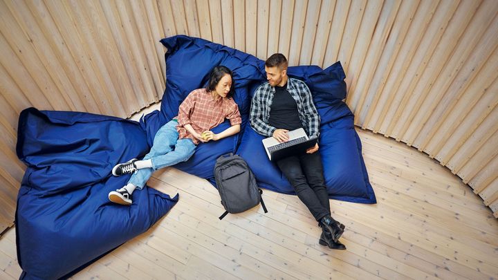 Kaksi henkilöä makoilee isoilla sinisillä säkkituoleilla puisessa huoneessa keskustellen rennosti.