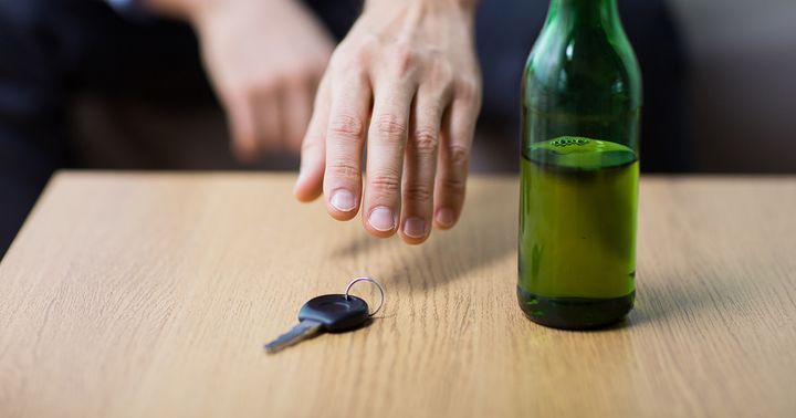 Käsi tavoittelee auton avainta, vieressä pöydällä pullollinen alkoholijuomaa.
