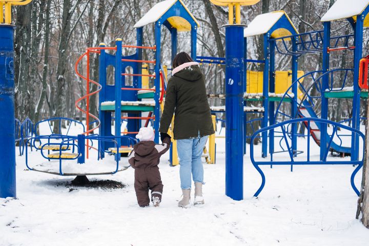 Aikuinen ja lapsi kävelevät talvisella leikkikentällä.