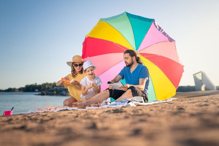 Father, mother, and child in the sun on a sandy beach, sheltered under a sun umbrella.