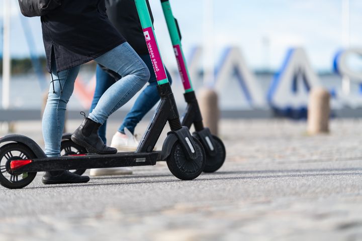 Kaksi henkilöä ajamassa sähköpotkulaudoilla kadulla. Taustalla meri ja Vaasa-kyltti.