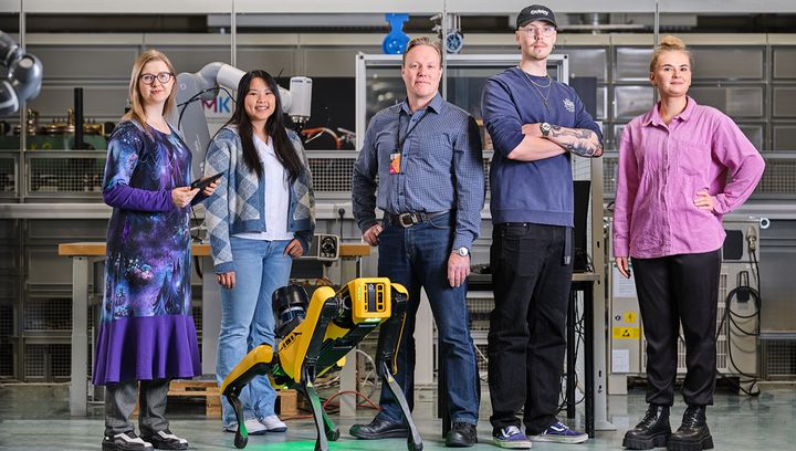 Agroup of five people stand together in Technobothnia teachning and research laboratory with a robot dog by their side.