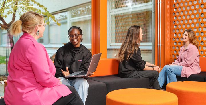 Four people sitting and talking in VAMK's modern and colorful lounge area.