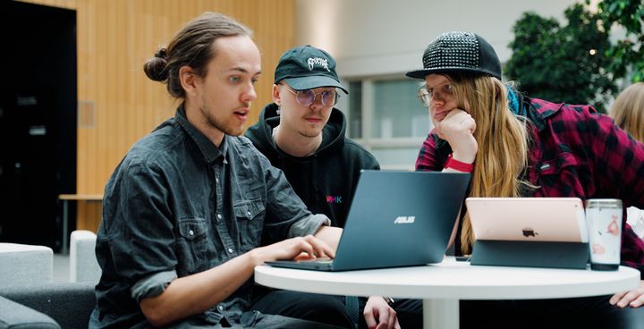 Kolme opiskelijaa kokoontuneena pöydän ääreen ja työskentelemässä kannettavilla tietokoneilla.