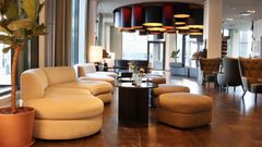 Hotellin aulassa on modernia ja mukavaa kalustusta, kuten pehmeitä sohvia ja pyöreitä tuoleja. Avarassa tilassa on myös kasveja sekä katossa näyttävä valoinstallaatio, jonka värimaailma tukee uutta sisustusta.