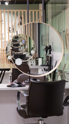 Kampaamon sisustus, jossa näkyy pyöreä peili, tuoli ja kampaamovälineitä.