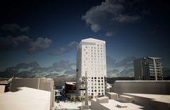 Havainnekuva: Korkea, moderni hotellirakennus kaupunkiympäristössä, taustalla vuoria ja pilvinen taivas.