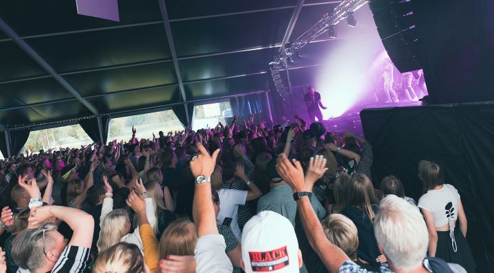 Ihmisjoukko konserttiteltassa, lavalla esiintyjä valojen loisteessa.