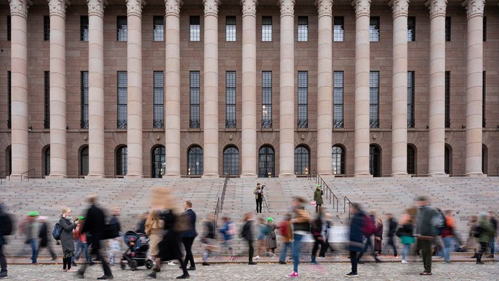 Ohikulkevia, liikkuvia ihmisiä eduskuntatalon portaiden alapuolella.