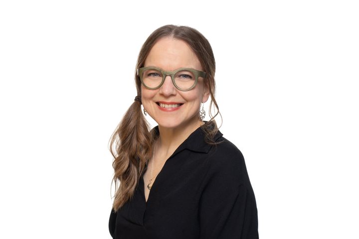 Personen ler mot kameran. Svart tröja och glasögon.